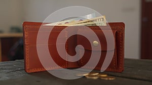 Brown bifold wallet with coin pocket and cardholder and cash is on dark wooden table in leather workshop. Pouch, money