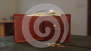 Brown bifold wallet with coin pocket and cardholder and cash is on dark wooden table in leather workshop. Pouch, money