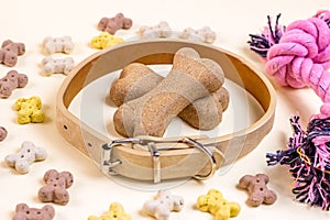 Brown biscuit bones for dogs with bright pink toy and beige collar on light background. Dog and puppy food, healthy treats.