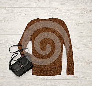 Brown-black sweater and black bag on a wooden background. Fashion concept. top view