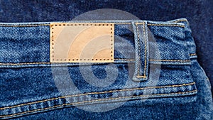 Brown blank leather label tag on denim pants background. Blank mockup beige leather label. Blue denim jeans with emty