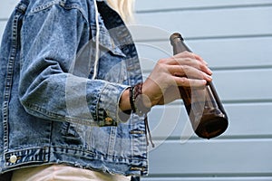 A brown bottle of beer in a hand of punk, informal woman, alcohol addiction, overdosage and abuse concept