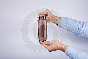 Brown bottle of shampoo or lotion in male hand on white background. Copy space, mock up