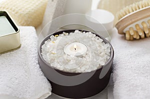 Brown bowl full of sea salt for bath procedures, candle flame, towels and other accessories for relaxation