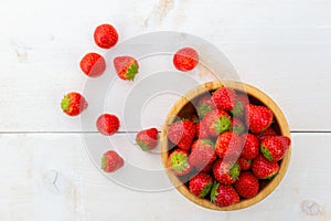 Brown bowl full strawberries on white wooden table from above.