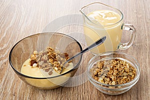 Brown bowl with muesli and yogurt, teaspoon, jug of yogurt, bowl with granola on table