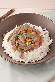 A brown bowl of white rice with stir fry beef with