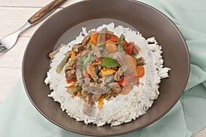 A brown bowl of white rice with stir fry beef with