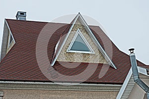Brown brick attic with one triangular window on the tiled roof of a private house