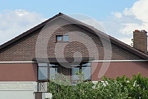 Brown brick attic of a private house with an iron balcony with windows