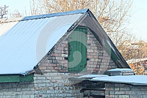 Brown brick attic of a rural house with a green wooden door