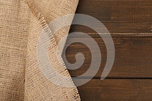 Brown burlap fabric on wooden table, top view. Space for text