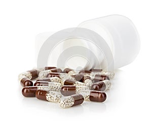 Brown capsules, pills poured out of a white bottle close-up on a white background.