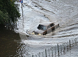 A brown car passes through a flooded road area after heavy rain