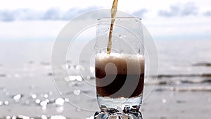 Brown carbonated drink in a beautiful glass at sunset by the sea and in a cafe