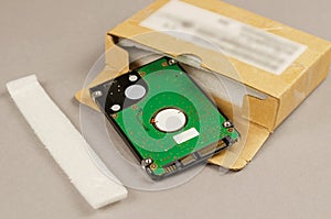 Brown cardboard box and internal computer hard drive on gray bac