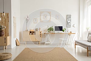 Brown carpet between pouf and grey sofa in white home office int photo