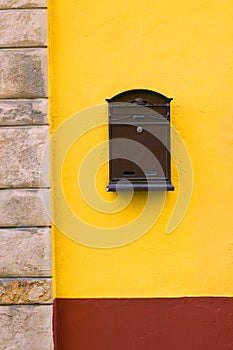 Brown cast-iron mail slot attached on a yellow wall