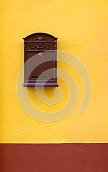 Brown cast-iron mail slot attached on a yellow wall