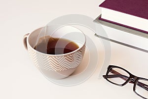 Brown ceramic cup with tea and paper tea bags, Reading Glasses and books on table.