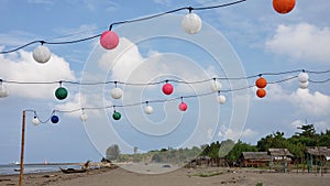 Brown chairs and colorful decorative lights on the beach with clouds in the blue sky as a background