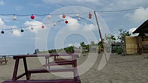 Brown chairs and colorful decorative lights on the beach with clouds in the blue sky as a background