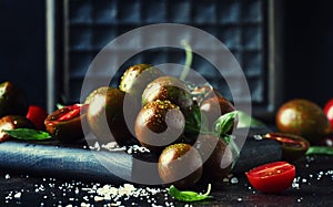 Brown cherry tomatoes with sea salt and green basil on dark table, autumn harvest, selective focus