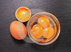 Brown chicken egg and egg yolks in glass bowl on natural stone black board. Flat lay