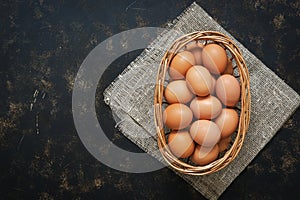 Brown chicken eggs in a basket on a dark rustic background, copy space, top view.