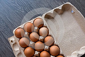 Brown chicken eggs in a box made of recycled cardboard are located on a brown wooden countertop in the kitchen. Top view