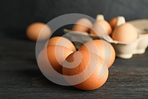 Brown chicken eggs in carton box on wooden table against black background, space for text