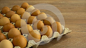 Brown chicken eggs in gray carton package box on wooden table