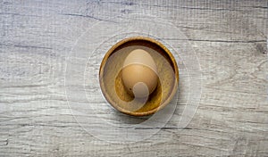 Brown chicken hen egg in brown wooden bowl on wooden table, top view angle of shooting with copy space