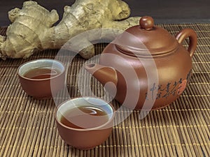 Brown chinese tea set of a teapot and cups and ginger on bamboo table mat .