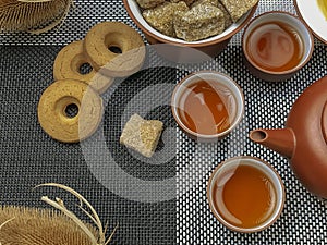 Brown chinese tea set of a teapots and three cups, cookies and brown sugar on bamboo table mat .