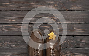 Brown classic leather men`s shoes and autumn golden leaves on dark wooden background top view. Autumn Fashion Concept. Fashionabl