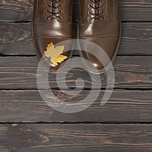 Brown classic leather men`s shoes and autumn golden leaves on dark wooden background top view. Autumn Fashion Concept. Fashionabl