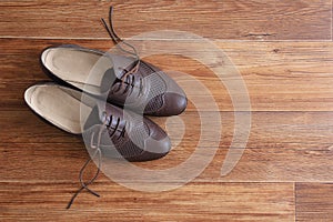 Brown classic women shoes with untied laces on a wooden floor.