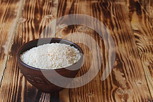 A brown clay bowl with round rice on a brown wooden table