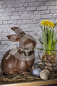 brown clay easter bunny in wooden bowl with easter eggs and hay