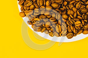 Brown coffee beans on a plate. heap of whole coffee beans on yellow background. copy space