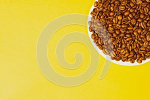 Brown coffee beans on a plate. heap of whole coffee beans on yellow background. copy space