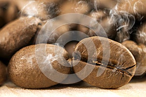 Brown coffee beans with white smoke vapour on yellow textured wooden board background close up.