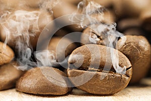 Brown coffee beans with white smoke vapour on yellow textured wooden board background close up.