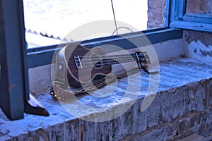 Brown colored ukulele with strap leaning against a brick window frame. Concept instruments, music, strings