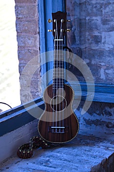 Brown colored ukulele with strap leaning against a brick window frame. Concept instruments, music, strings