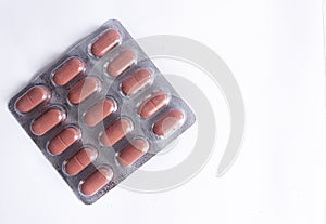Brown coloured pills in plastic packaging on white background