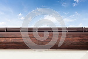 Brown copper gutter under a cloudy blue sky.