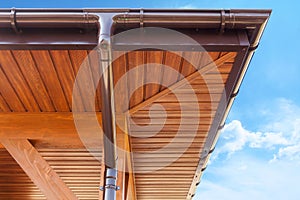 Brown copper gutter under a cloudy blue sky.