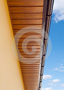 Brown copper gutter under a cloudy blue sky.